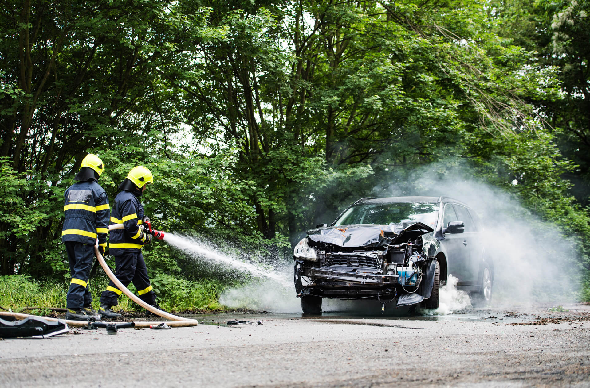 Two firefighters extinguishing a burning car after an accident