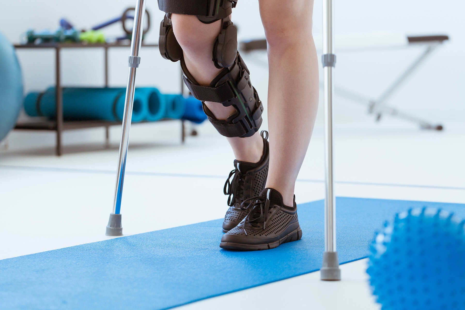 Injured patient in a leg brace exercising on a blue mat in a phy