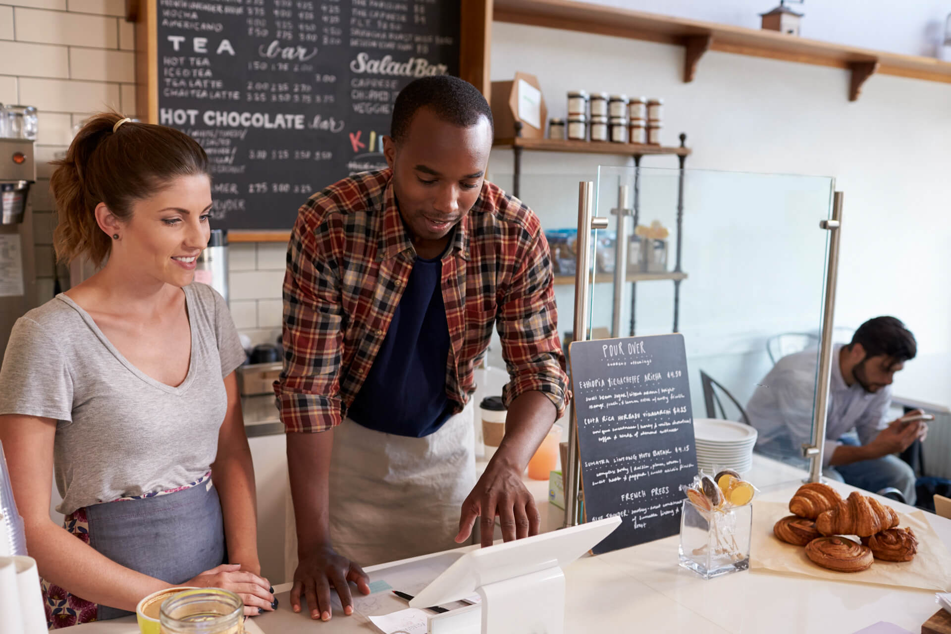 Barista at coffee shop showing till to new employee