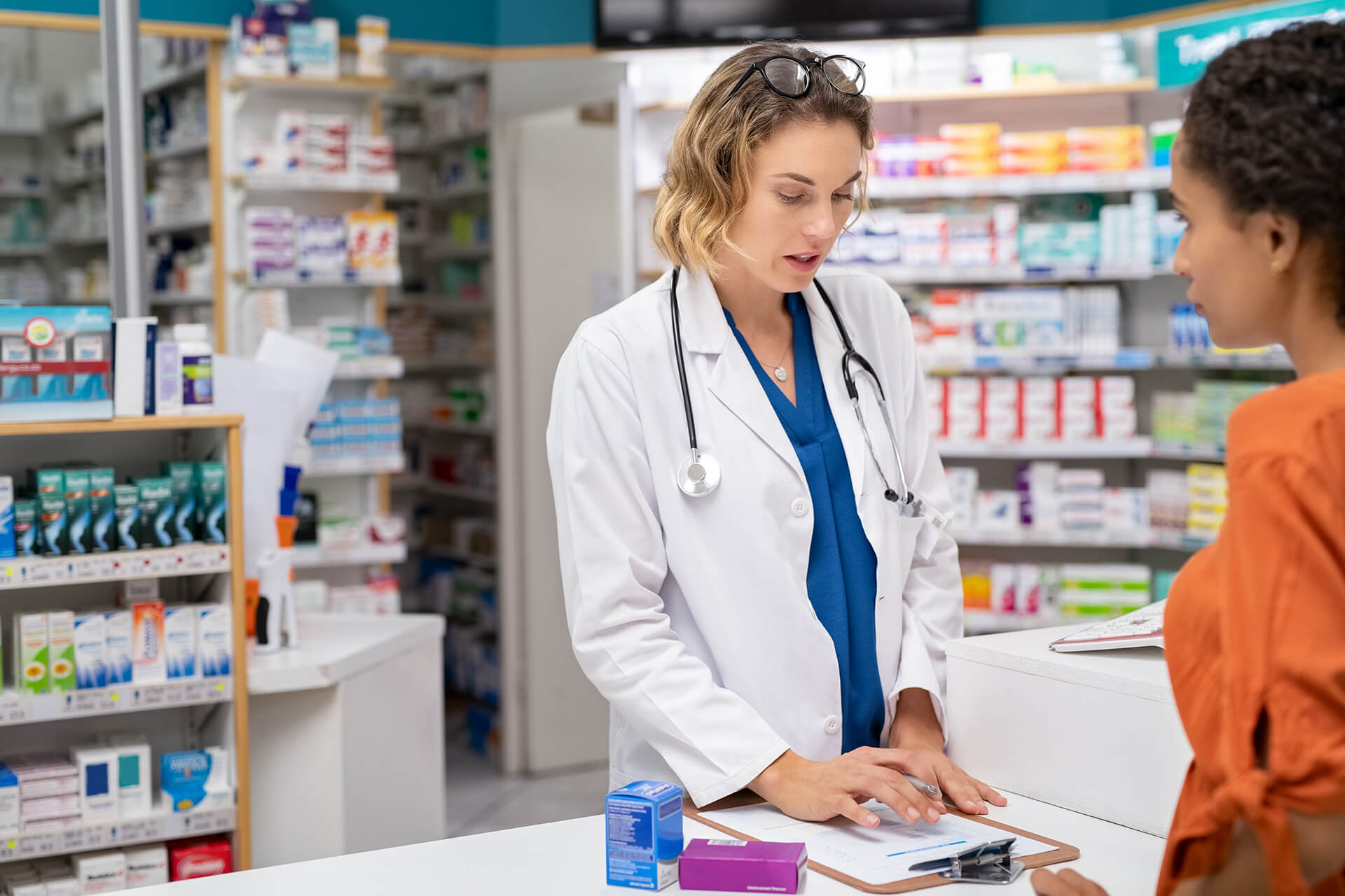 Woman pharmacist with prescription assisting a customer standing at the counter. Doctor  in drugstore suggesting medical drug to buyer. Druggist with prescription assisting and explaining dosage of medicines to young african woman with copy space.