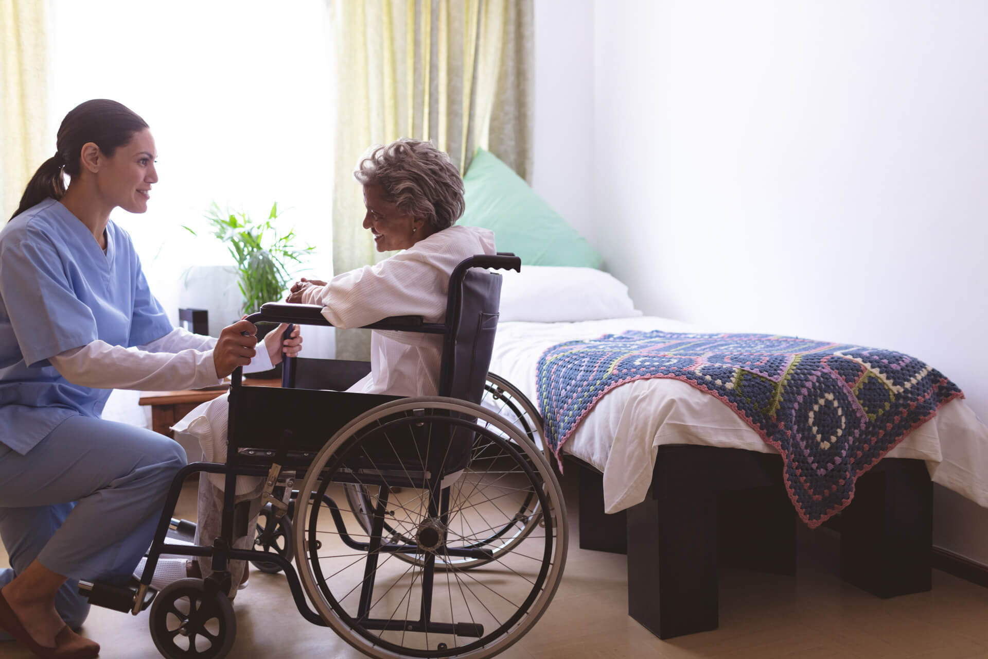 Side view of nurse talking with senior mixed race female patient at nursing home. Senior female sits in a wheelchair.